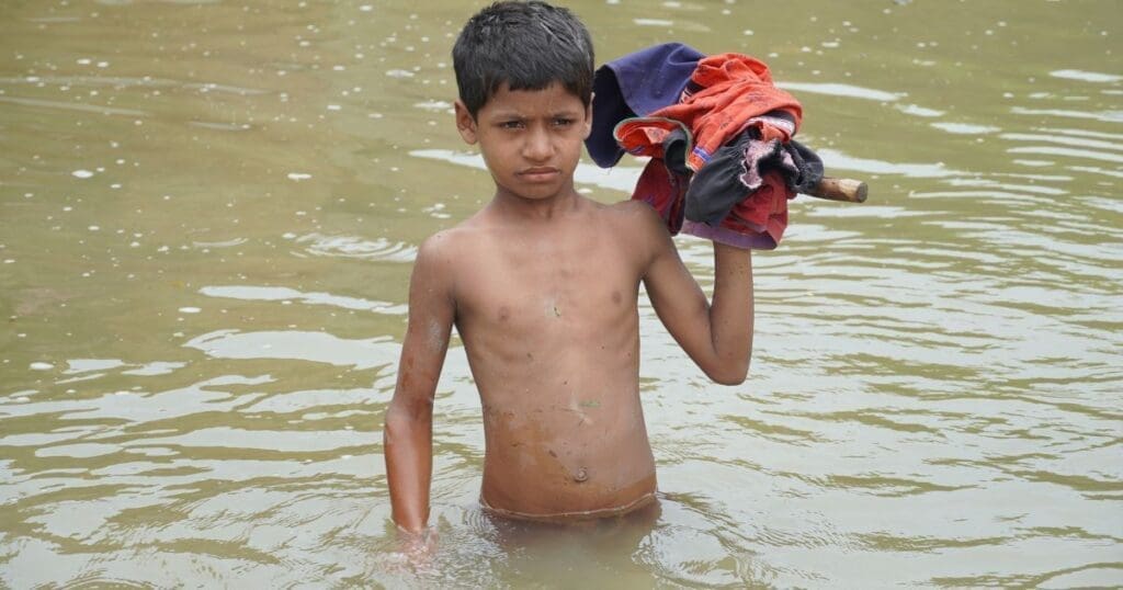 Boy wading through floodwater carrying clothes